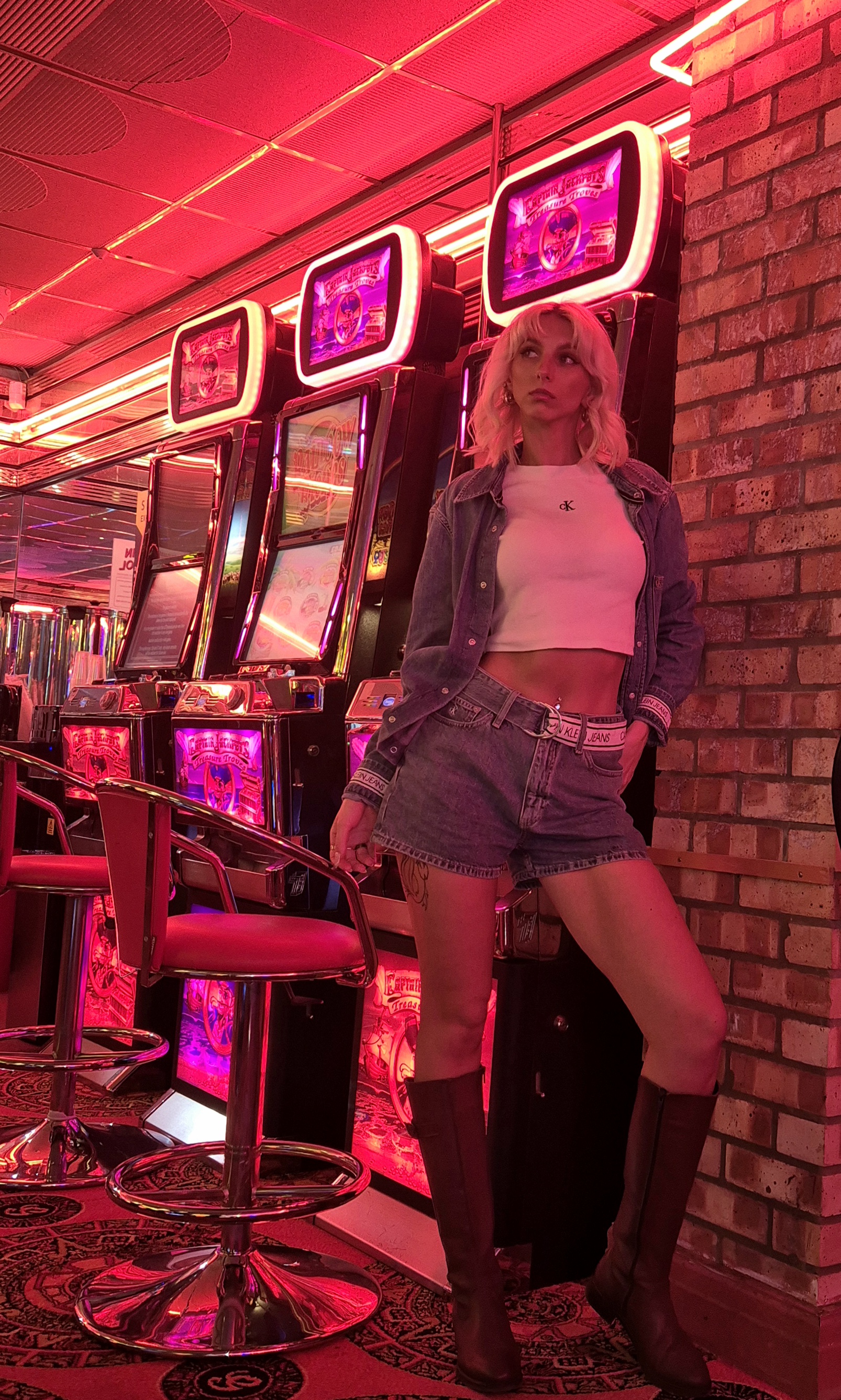 Emma Townsend posing under pink neon arcade lights in a denim outfit